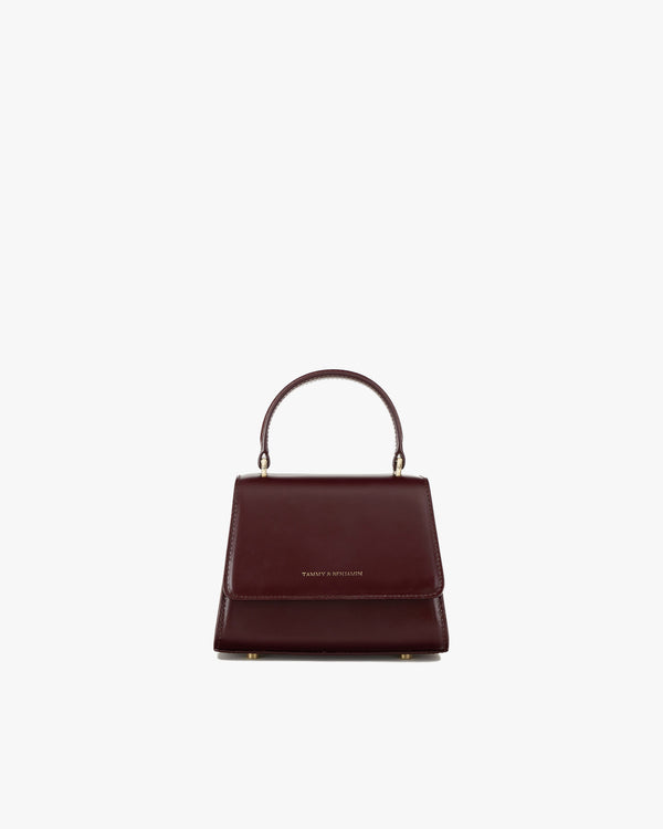 Sac ALEXIA NANO Mahogany de face, rabat fermé, poignée rigide relevée, posé sur fond blanc