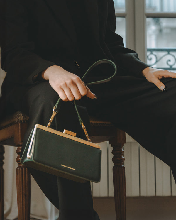 Bandoulière courte vert émeraude tenue en main, fixée au sac posé sur un tabouret