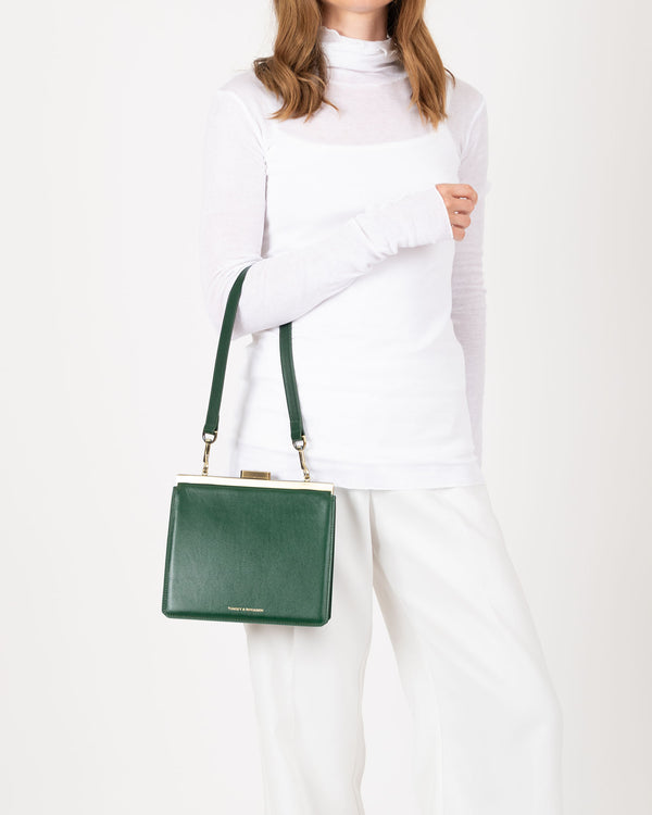 JEANNE bag in emerald green worn on the shoulder with strap, gold metal clasp visible