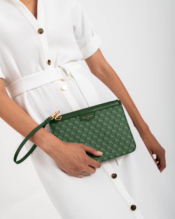 Pochette PM Monogram verte tenue à la main par sa dragonne, portée à la taille sur robe blanche