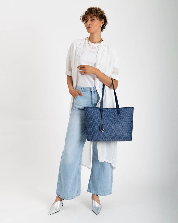 TOTE MONOGRAM bleu, porté à la main par une femme, en toile enduite à motif