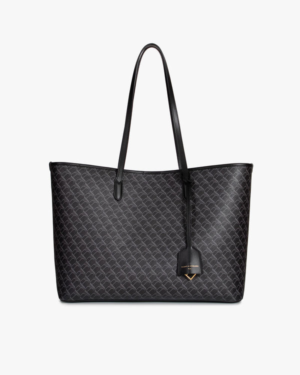 Sac TOTE MONOGRAM noir, vue de face, posé, anses longues en cuir et pampille logo