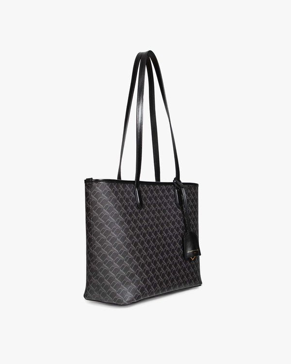 Sac TOTE MONOGRAM PM noir monogram, vue de profil, porté à l'épaule par ses anses plates en cuir