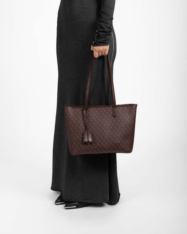 TOTE MONOGRAM PM chocolat, porté à la main, vue de profil sur modèle en robe noire