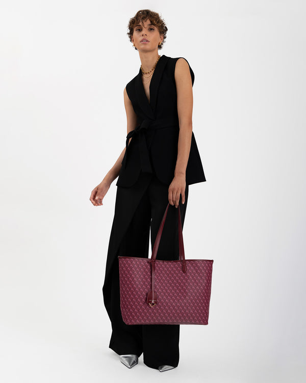 TOTE MONOGRAM Bordeaux porté à la main, vue de face sur mannequin en tenue noire