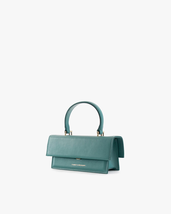 Sac THEA MINI turquoise de trois quarts, rabat fermé, poignée haute, fond blanc