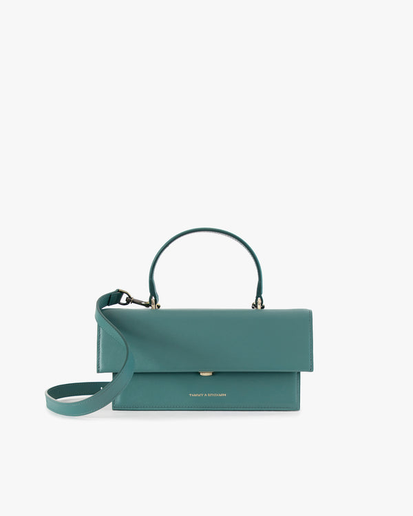 Sac THEA Turquoise de face, rabat fermé, poignée rigide et bandoulière en cuir détachée posée devant