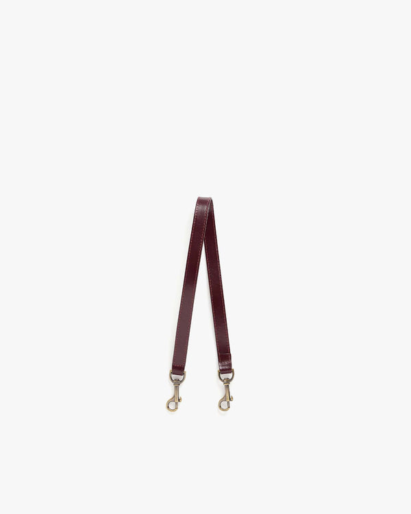 Bandoulière courte Mahogany en cuir, posée à plat, avec ses deux mousquetons en laiton vieilli