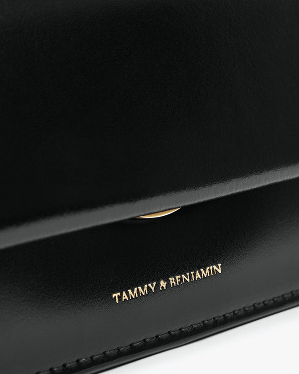 Sac THEA MINI noir, gros plan sur le rabat et le logo doré Tammy & Benjamin