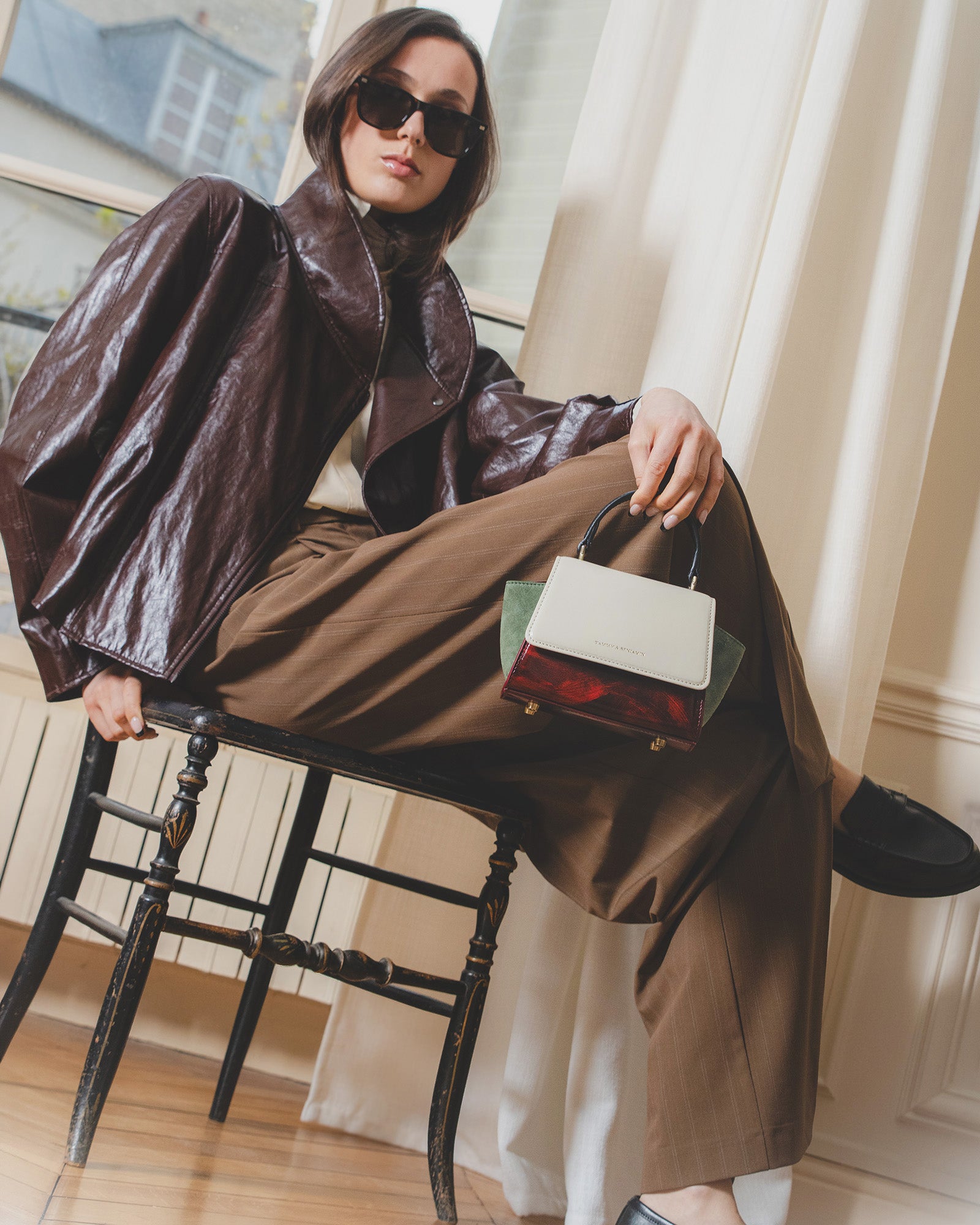 Sac ALEXIA NANO Colourblock art déco porté à la main, assise sur une chaise, gros plan sur la poignée