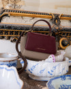 Sac ALEXIA NANO Colourblock Stratum, vue de face, poignée rigide, posé sur une coupe en porcelaine