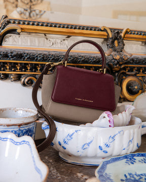 Sac ALEXIA NANO Colourblock Stratum, vue de face, poignée rigide, posé sur une coupe en porcelaine