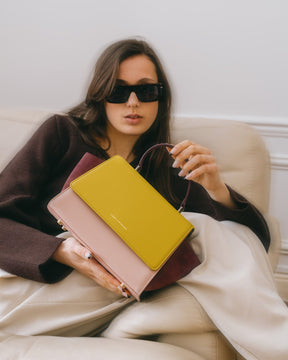 Sac ALEXIA Colourblock Vesper tenu à la main, porté assis sur un canapé, poignée gainée