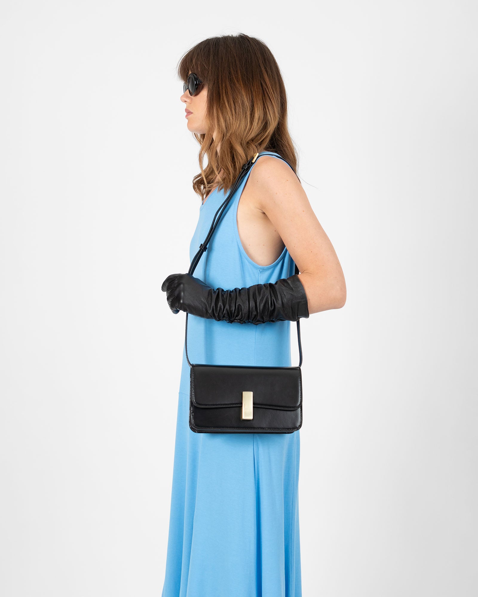 BLAKE bag in black, worn crossbody in profile view on model in blue dress, gold clasp visible