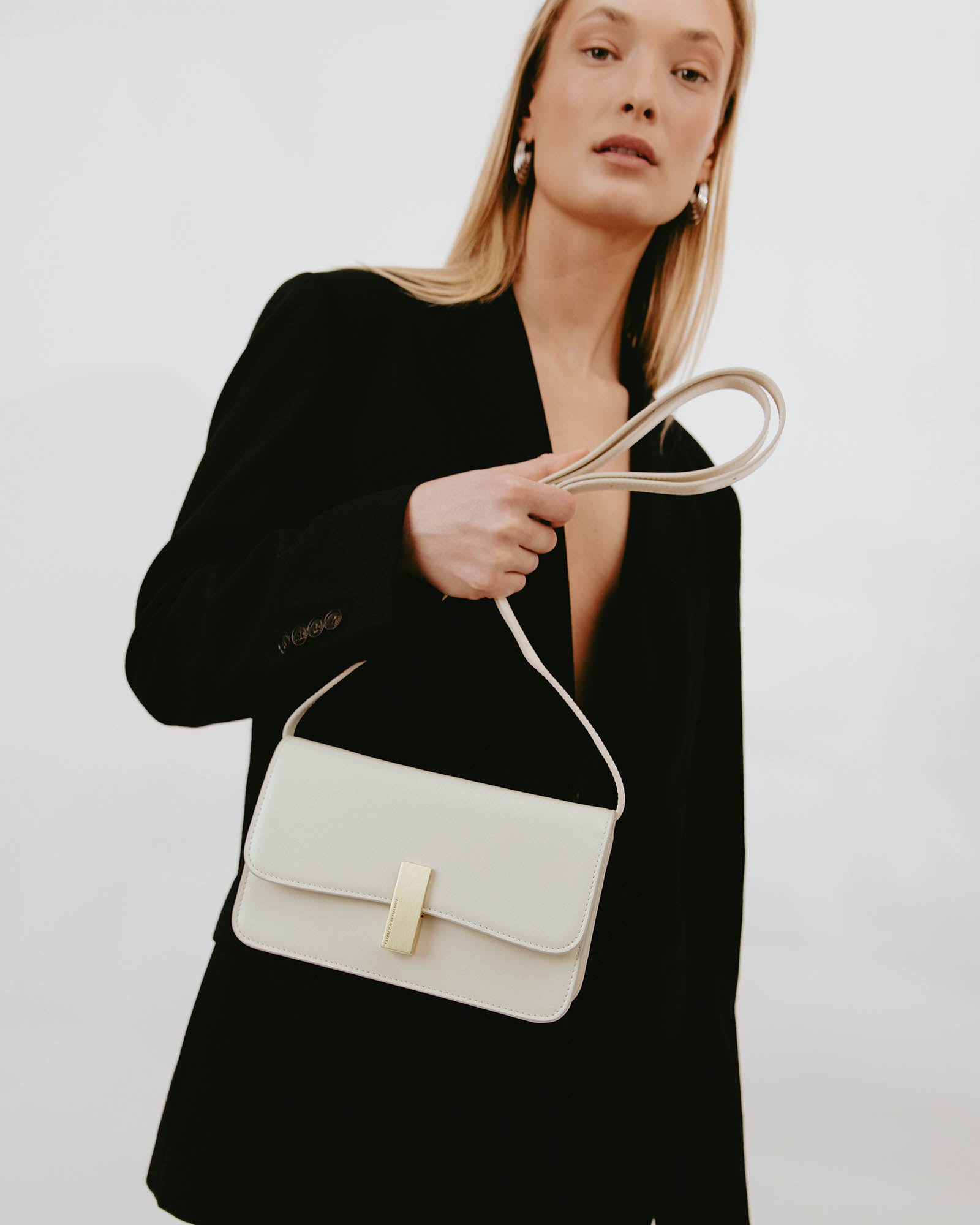 Sac BLAKE Ivoire tenu à la main par la bandoulière, porté avec un blazer noir