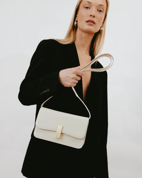 Sac BLAKE Ivoire tenu à la main par la bandoulière, porté avec un blazer noir