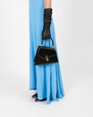 Sac CUBIST en cuir noir tenu à la main par une femme en gants longs, porté avec une robe bleue