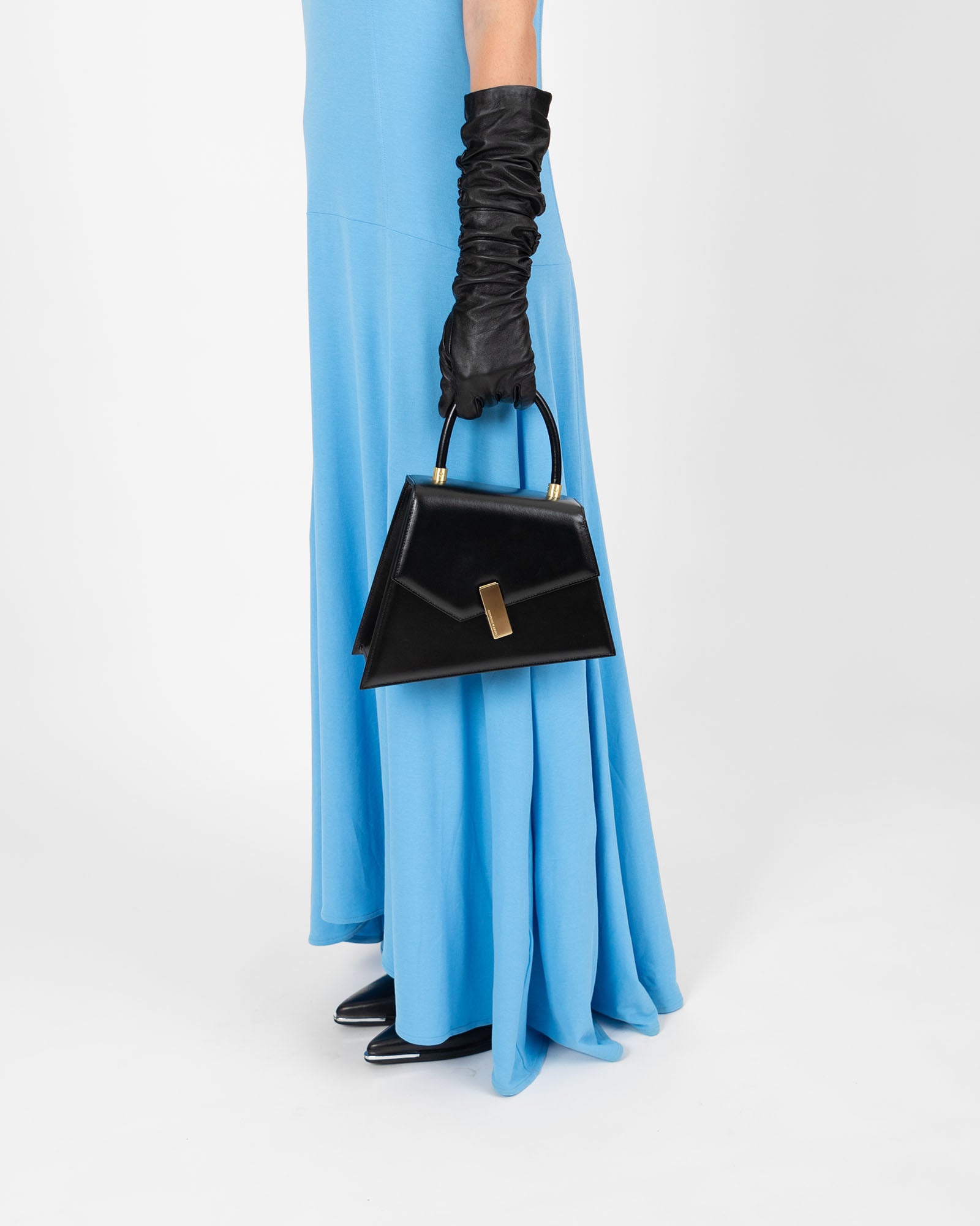 Sac CUBIST en cuir noir tenu à la main par une femme en gants longs, porté avec une robe bleue