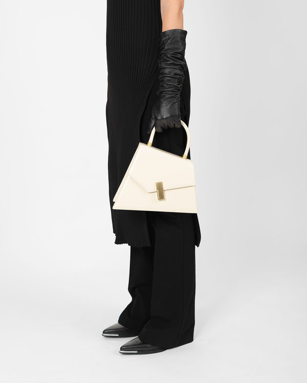 Sac CUBIST ivoire porté à la main par une silhouette en tenue noire, vue de profil