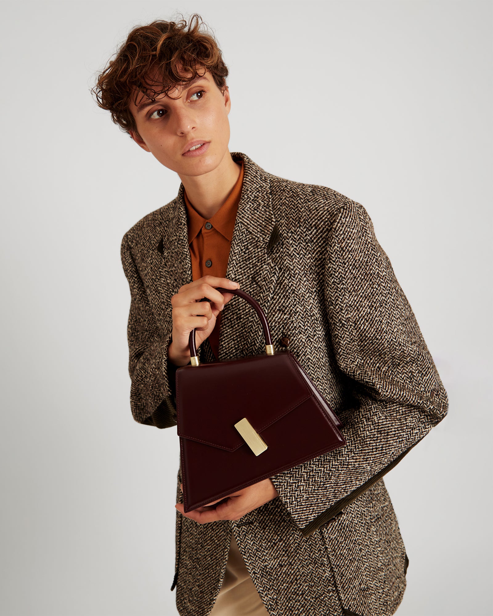 CUBIST bag in Mahogany held by hand, close-up on gold clasp and rounded handle