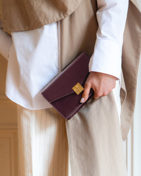ELEANOR Aubergine clutch held in hand, close-up of the gold Marble Arch clasp
