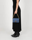 Sac ELEANOR bleu porté à la main, chaîne dorée, vue de profil sur modèle en robe noire