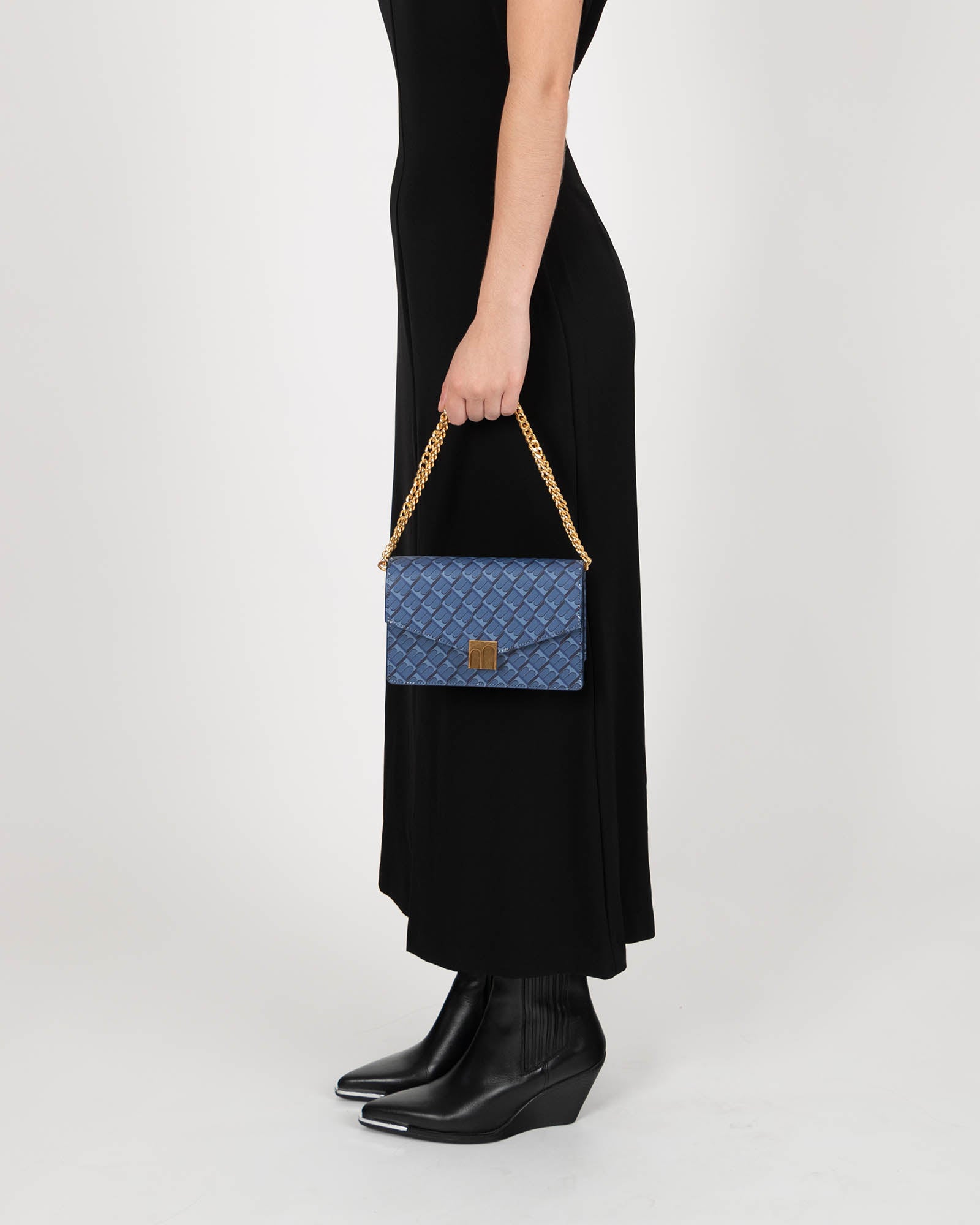 Sac ELEANOR bleu porté à la main, chaîne dorée, vue de profil sur modèle en robe noire