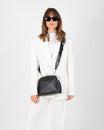 Sac EMMA noir porté en bandoulière croisée, fermoir doré, sur tailleur blanc