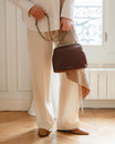 Sac EMMA brun tenu à la main par la chaîne, porté par une femme en pantalon à rayures