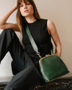 Sac EMMA vert émeraude porté en bandoulière avec anse longue, fermoir doré, assise sur rebord en marbre