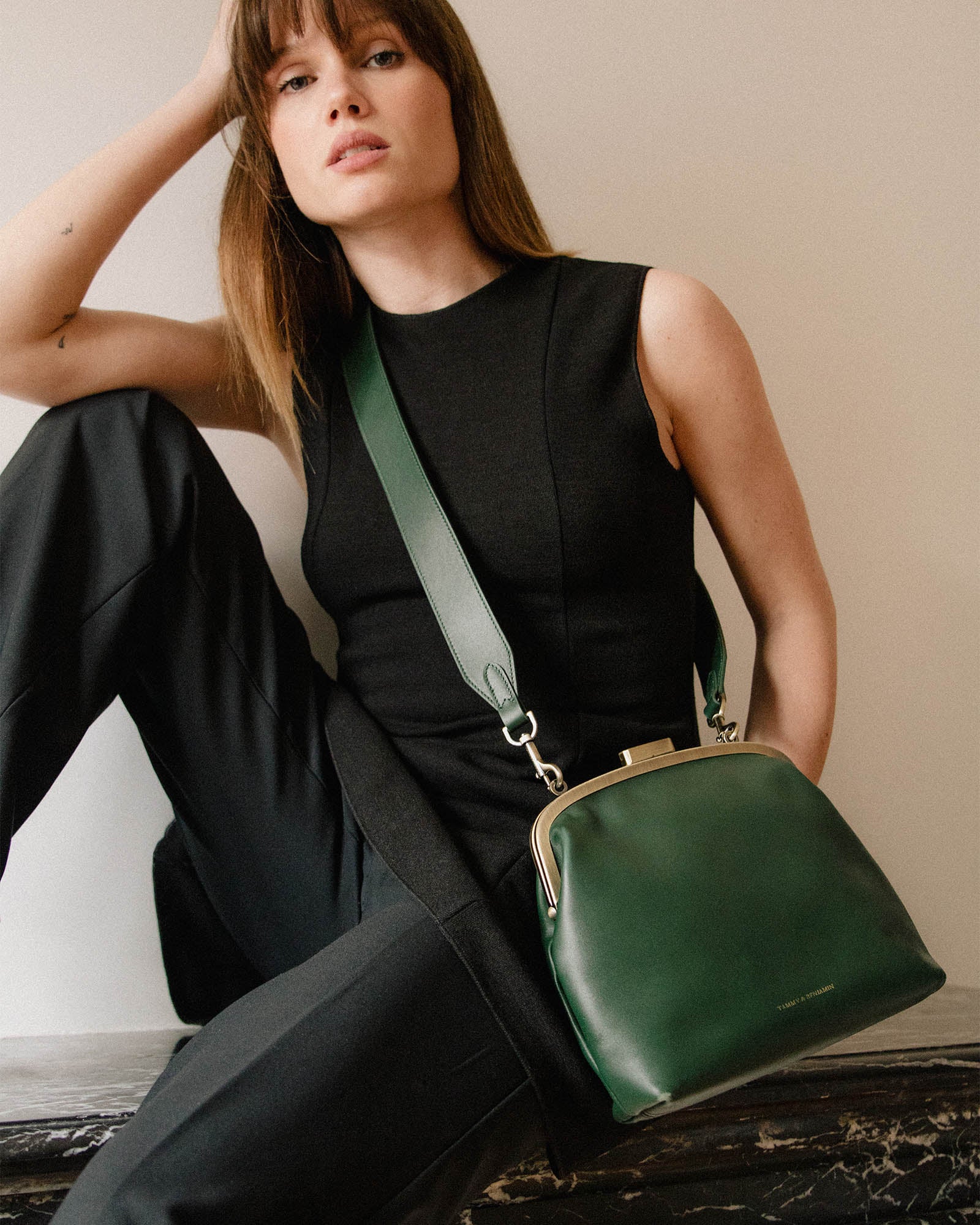 Sac EMMA vert émeraude porté en bandoulière avec anse longue, fermoir doré, assise sur rebord en marbre