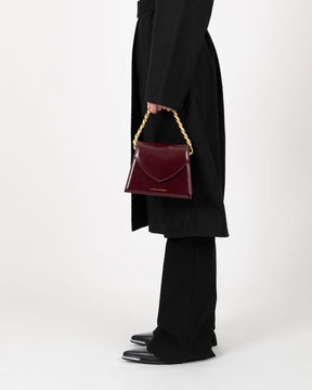 Sac GABRIELLE Mahogany porté à la main par la anse chaîne dorée, vue de profil