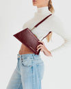 JAY bag in Bordeaux naplak, held in hand with shoulder strap, side view over jeans