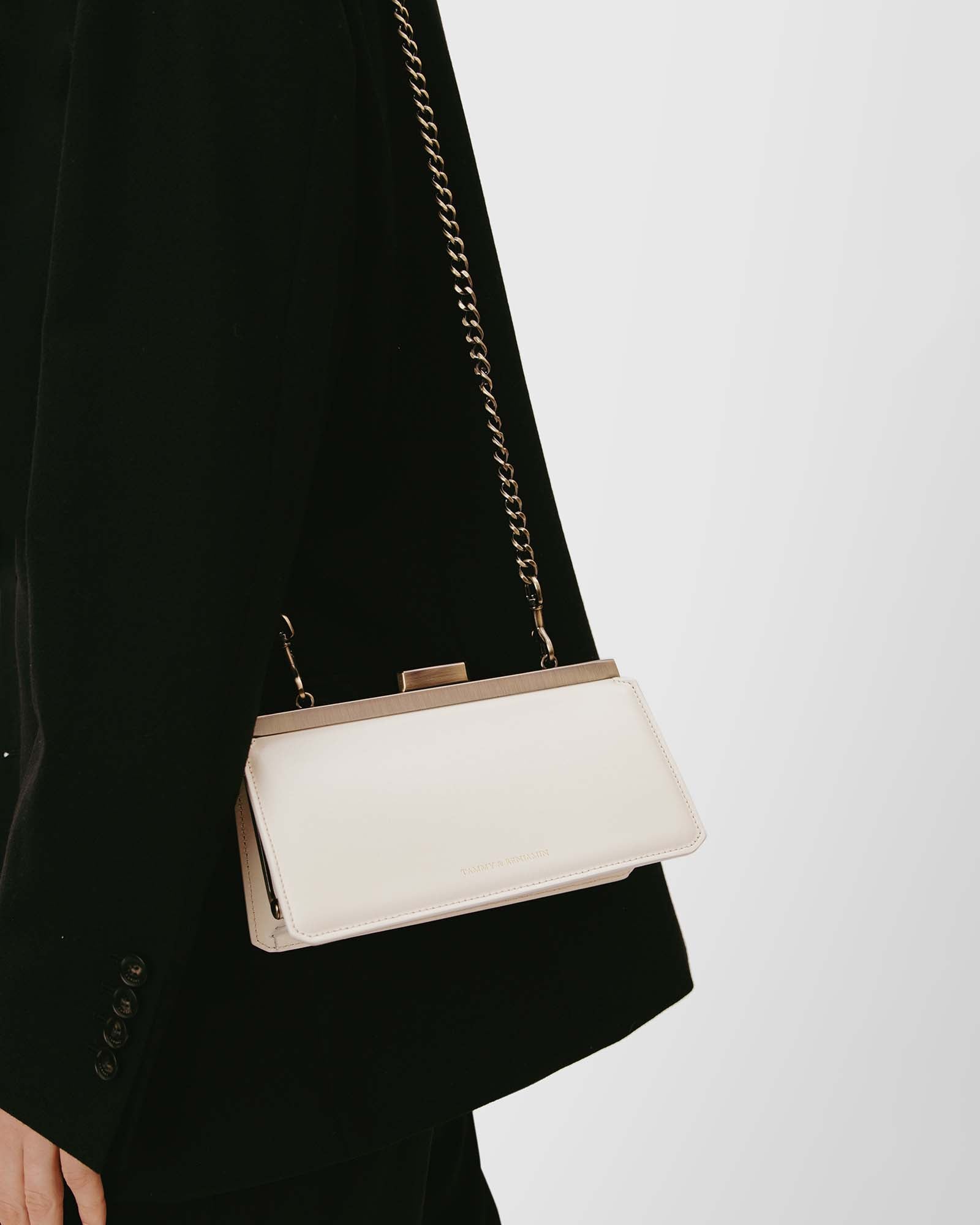 Sac JEANNE BAGUETTE Ivoire porté à l'épaule avec chaîne, détail du fermoir rétro, sur tailleur noir