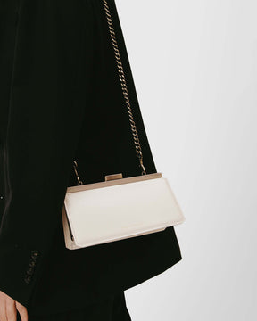 Sac JEANNE BAGUETTE Ivoire porté à l'épaule avec chaîne, détail du fermoir rétro, sur tailleur noir