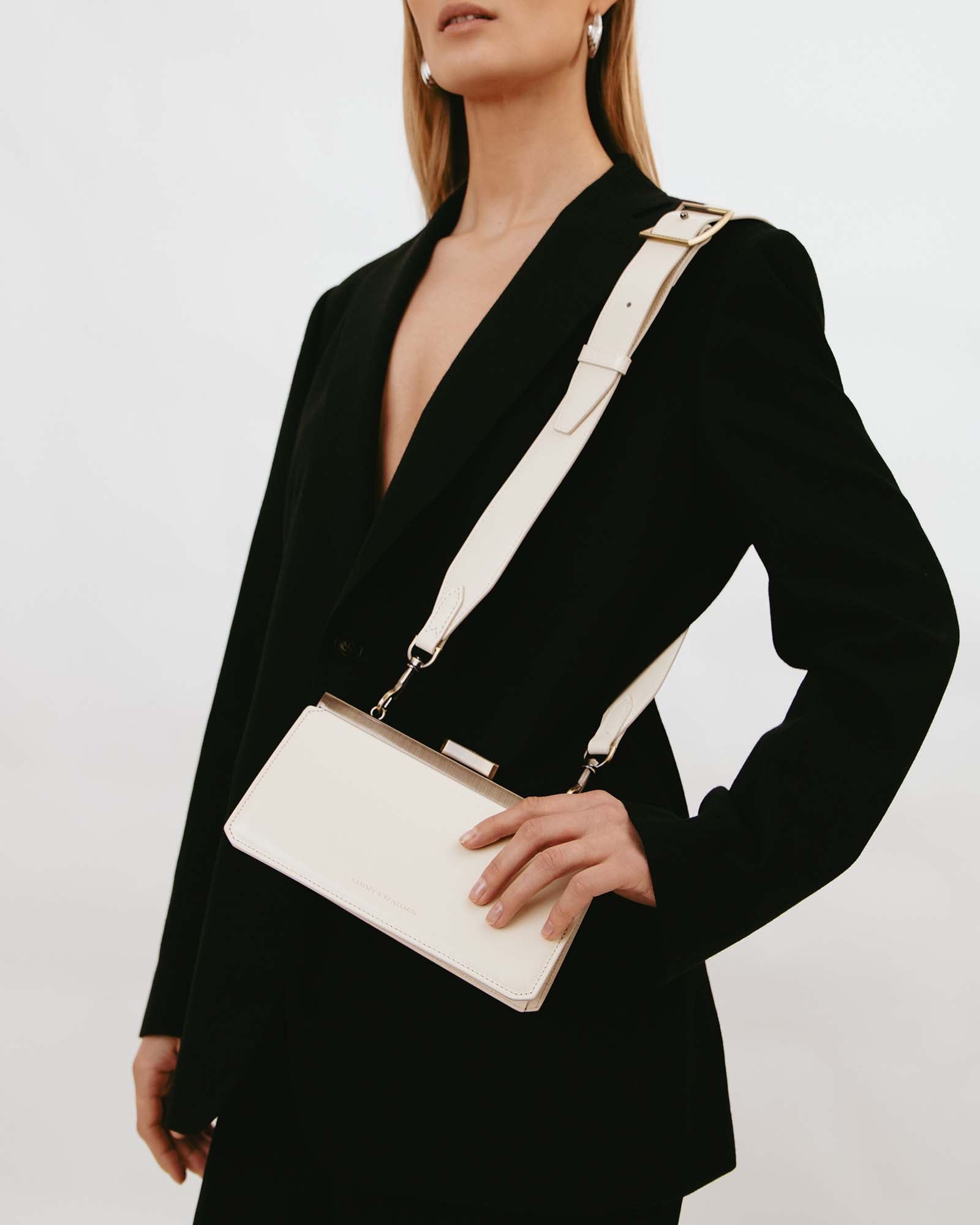 Sac JEANNE BAGUETTE Ivoire porté en bandoulière, fermoir rétro en gros plan sur blazer noir