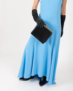 Sac JEANNE Noir tenu à la main par le fermoir métallique, porté avec une robe bleue