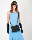 Sac JEANNE noir porté en bandoulière croisée, fermoir métallique, porté par une femme en robe bleue