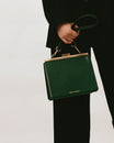 Sac porté main tenu par une personne, bandoulière courte vert émeraude en cuir, mousquetons laiton vieilli