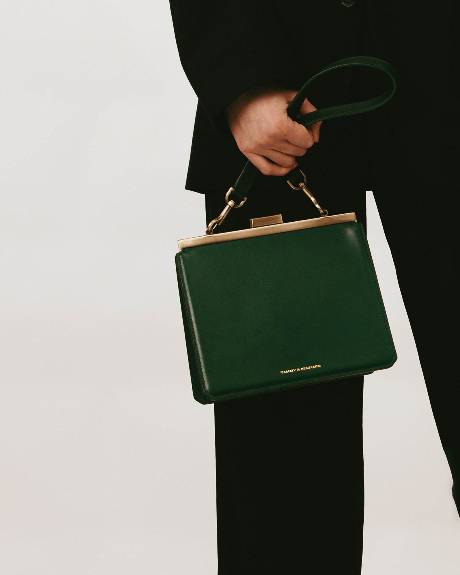 Sac porté main tenu par une personne, bandoulière courte vert émeraude en cuir, mousquetons laiton vieilli