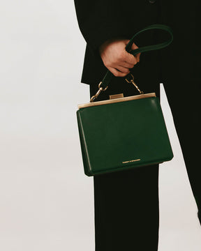 Sac porté main tenu par une personne, bandoulière courte vert émeraude en cuir, mousquetons laiton vieilli
