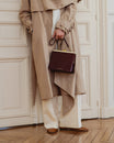 Sac JEANNE Mahogany porté à la main, fermoir doré, détail des finitions sur un trench beige