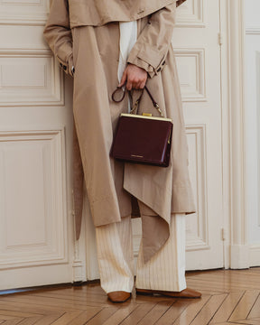 Sac JEANNE Mahogany porté à la main, fermoir doré, détail des finitions sur un trench beige