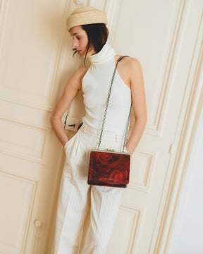 Sac JEANNE en cuir marbré rouge, porté en bandoulière avec chaîne, posé devant une porte