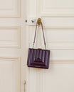 JUDE bag in quilted Mahogany hanging by its strap from an ornate brass door handle