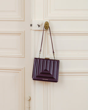 JUDE bag in quilted Mahogany hanging by its strap from an ornate brass door handle