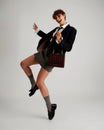 JUDE bag in quilted Mahogany, held by hand by a model mid-motion, detachable strap visible
