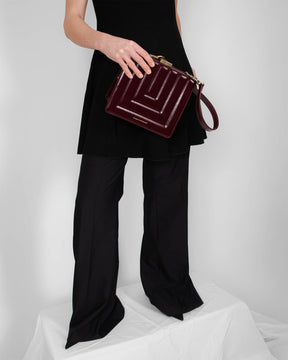 JUDE bag in quilted Mahogany, held by the handle, gold clasp detail, worn with a black outfit