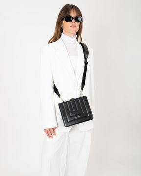 Sac JUDE noir matelassé porté en bandoulière, vue de face sur mannequin en tailleur blanc