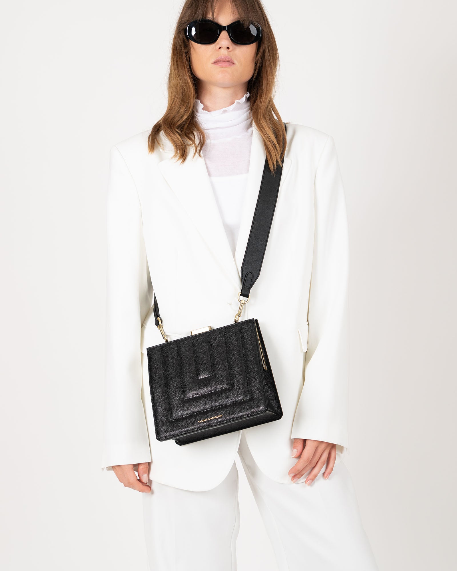 Sac JUDE noir matelassé porté en bandoulière, vue de face sur un tailleur blanc